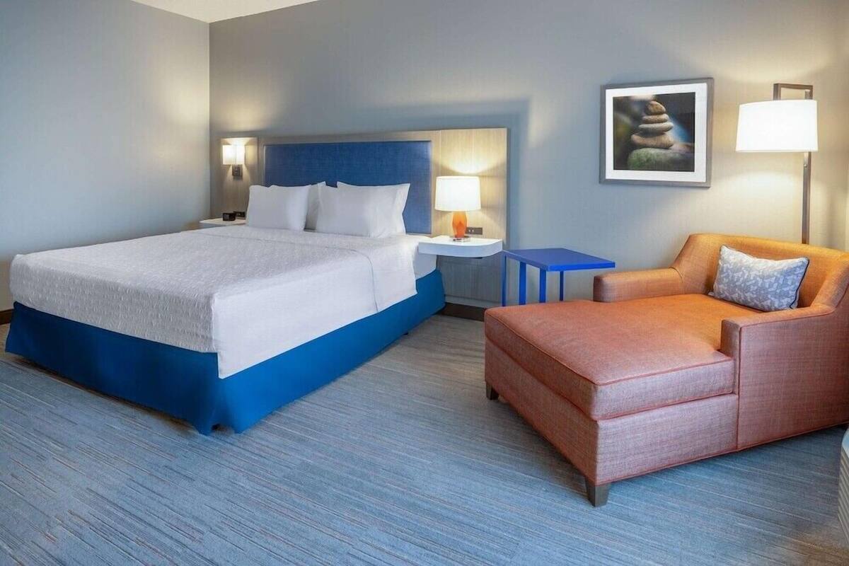 Ein Hotelzimmer mit Bett, Nachttisch, Tisch, Sofa und Wandlampe.