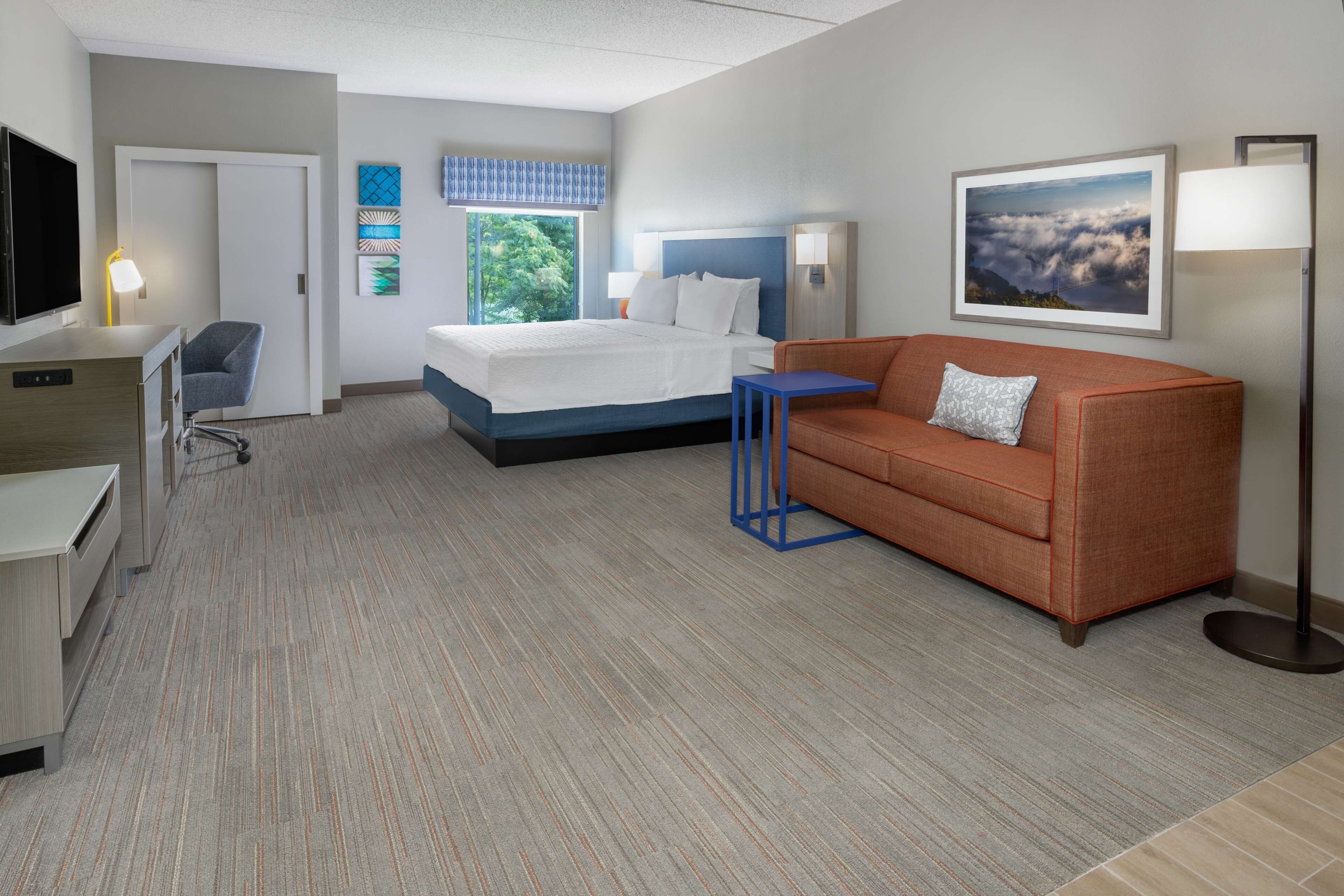 A hotel room with a bed, a sofa, a desk, a chair, and a TV.