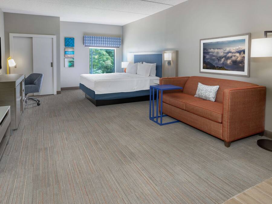 A hotel room with a bed, a sofa, a desk, a chair, and a TV.