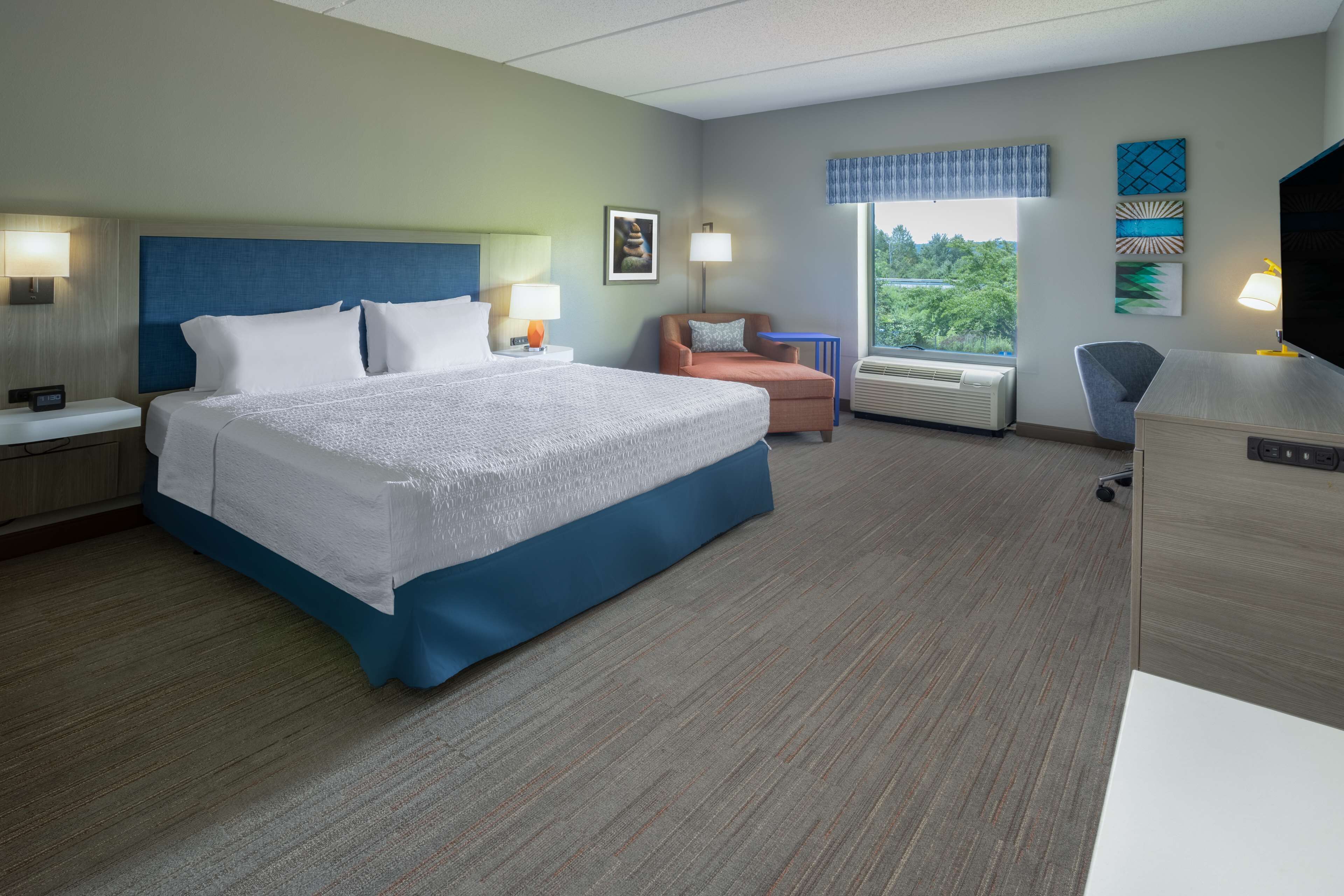 A hotel room with a large bed, a desk, a chair, and a TV.