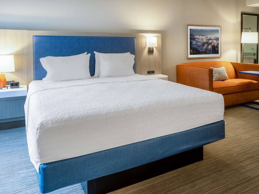 Une chambre d’hôtel avec un grand lit, une table de chevet avec une lampe, un canapé et un tableau encadré au mur.