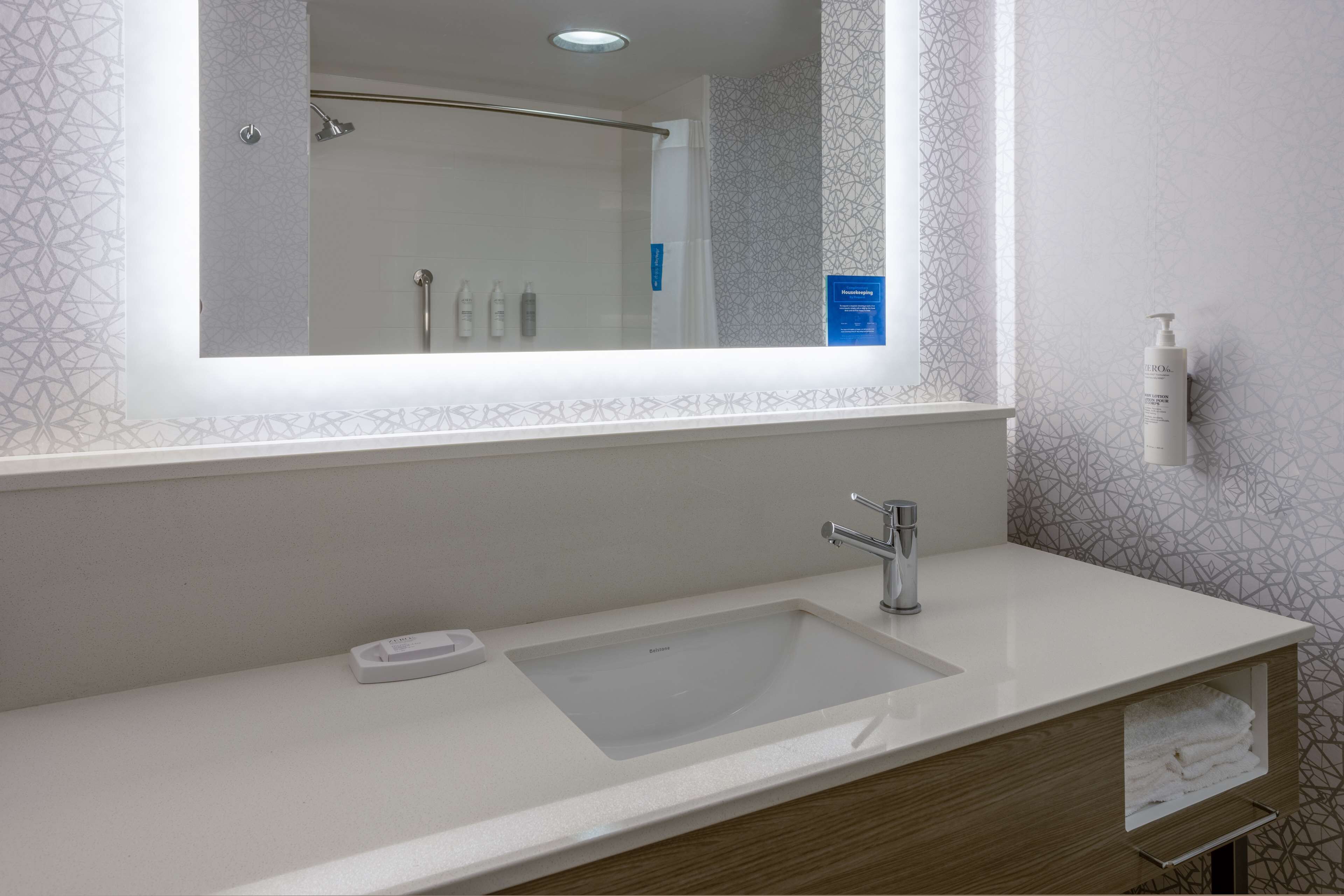 Un baño moderno con un espejo grande, un lavamanos rectangular y una ducha visible al fondo.