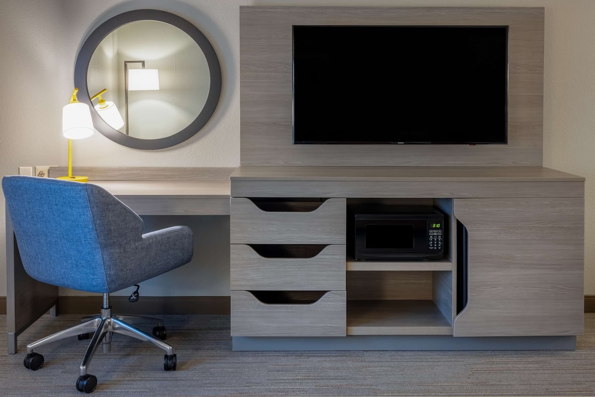 Ein modernes Hotelzimmer mit Flachbildfernseher, Schreibtisch mit Lampe, Stuhl und Mikrowelle.