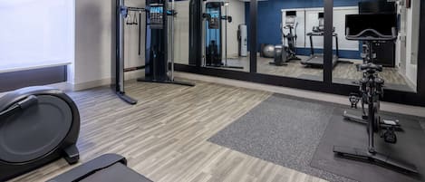 A gym with exercise equipment, a mirrored wall, and a treadmill.