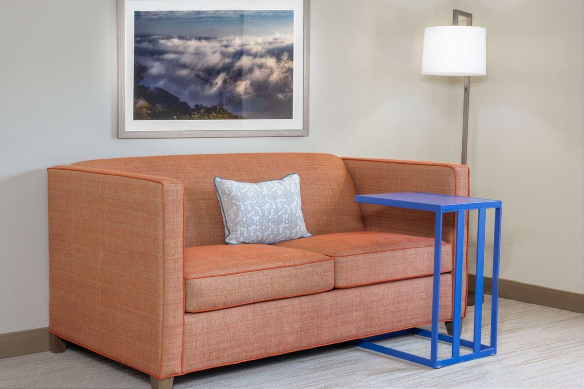 Ein Zimmer mit einer Couch, einem kleinen Tisch, einer Lampe und einem gerahmten Bild an der Wand.