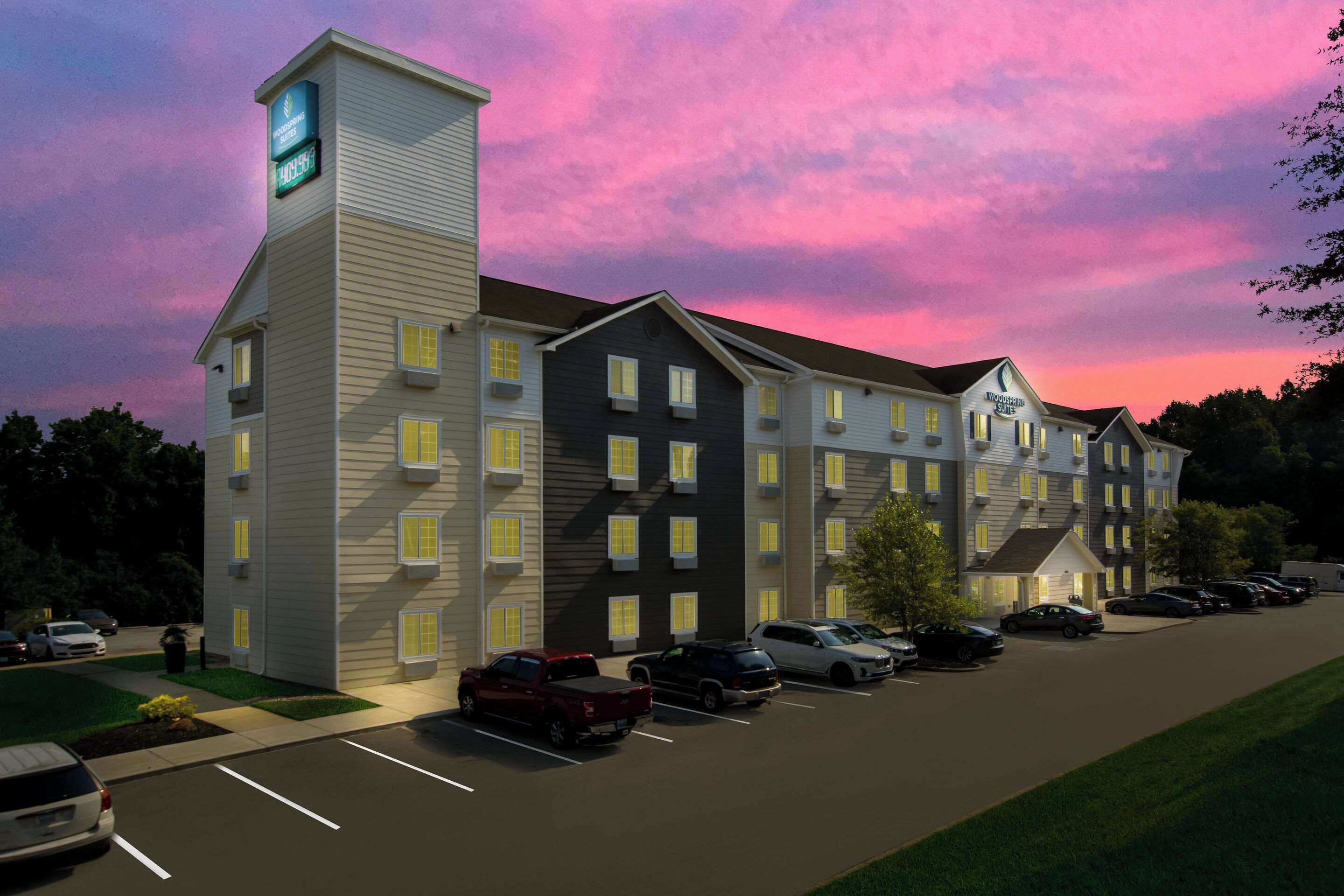 Un hôtel à plusieurs étages, doté d’une tour centrale, d’un parking et offrant une vue sur un ciel au coucher du soleil.