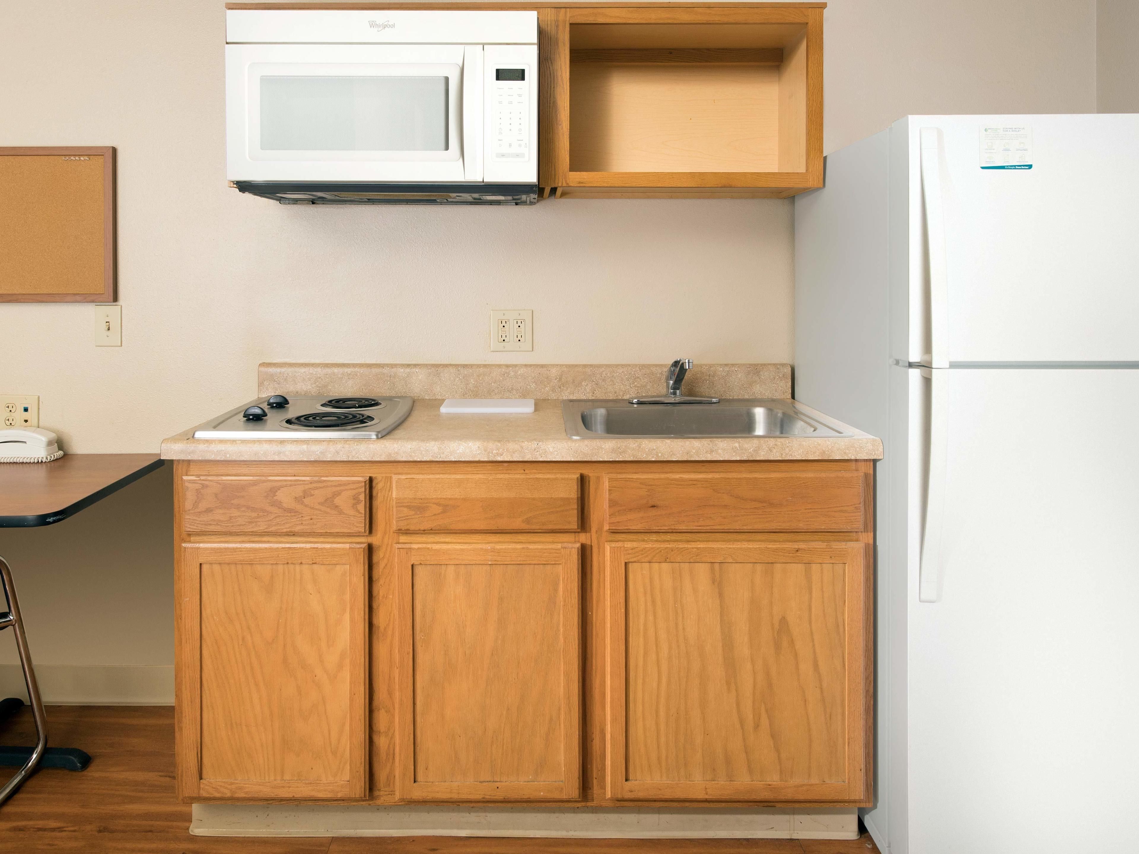 A kitchen with wooden cabinets, a white microwave, a stove, a sink, and a refrigerator.