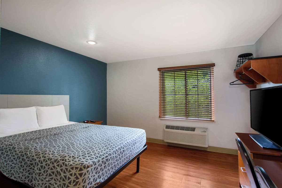 A bedroom with a bed, a TV, a heater, and a window with blinds.