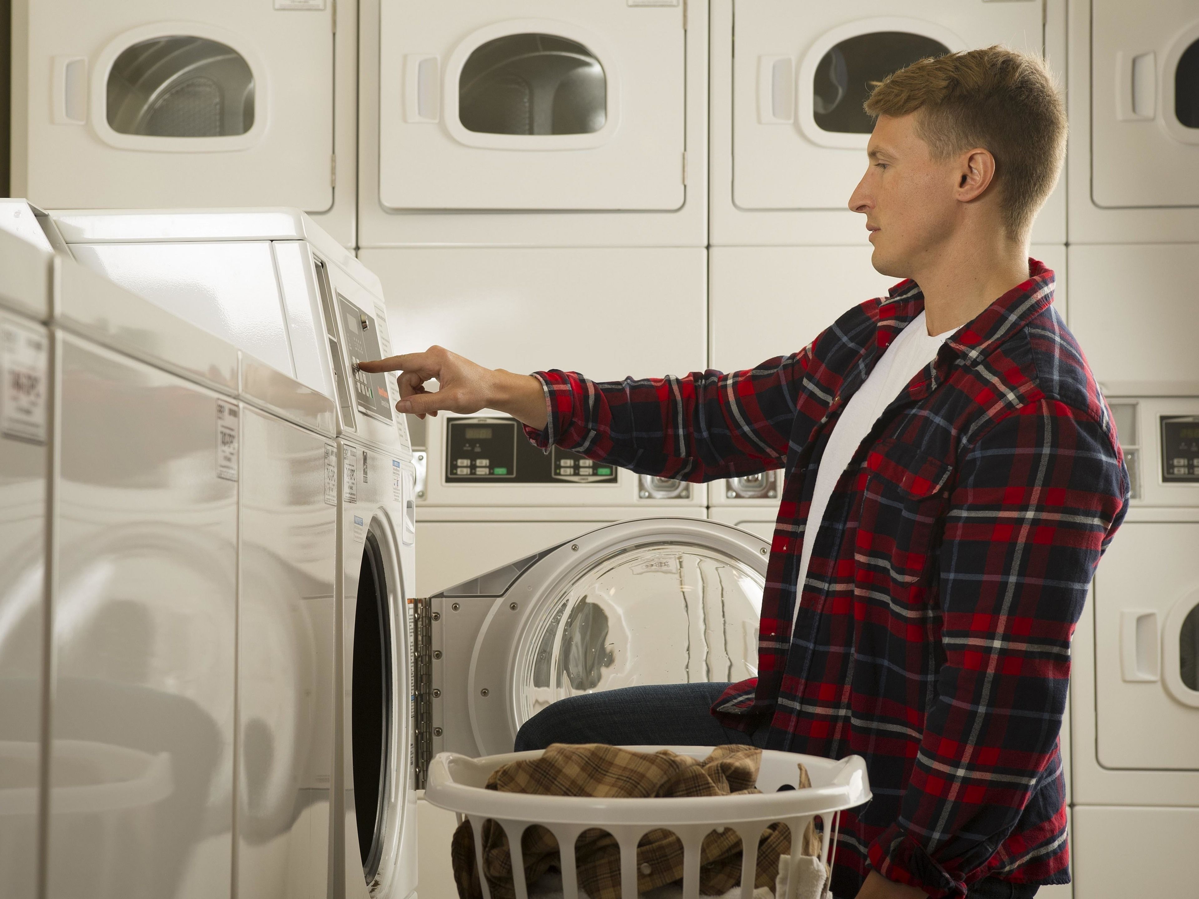 A person operating a front-loading washing machine in a laundromat with multiple machines.