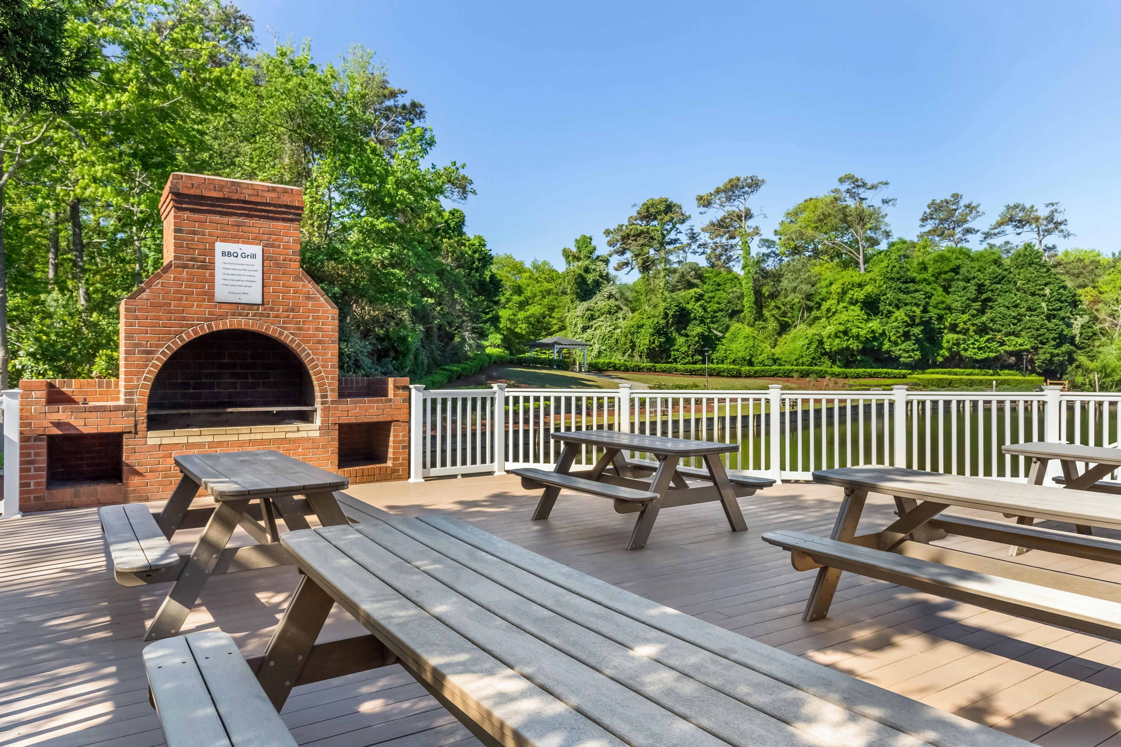 An outdoor BBQ grill area with picnic tables and a view of a lake.