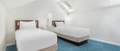 Une chambre d’hôtel avec deux lits, un ventilateur de plafond, une table de chevet avec une lampe et un puits de lumière.