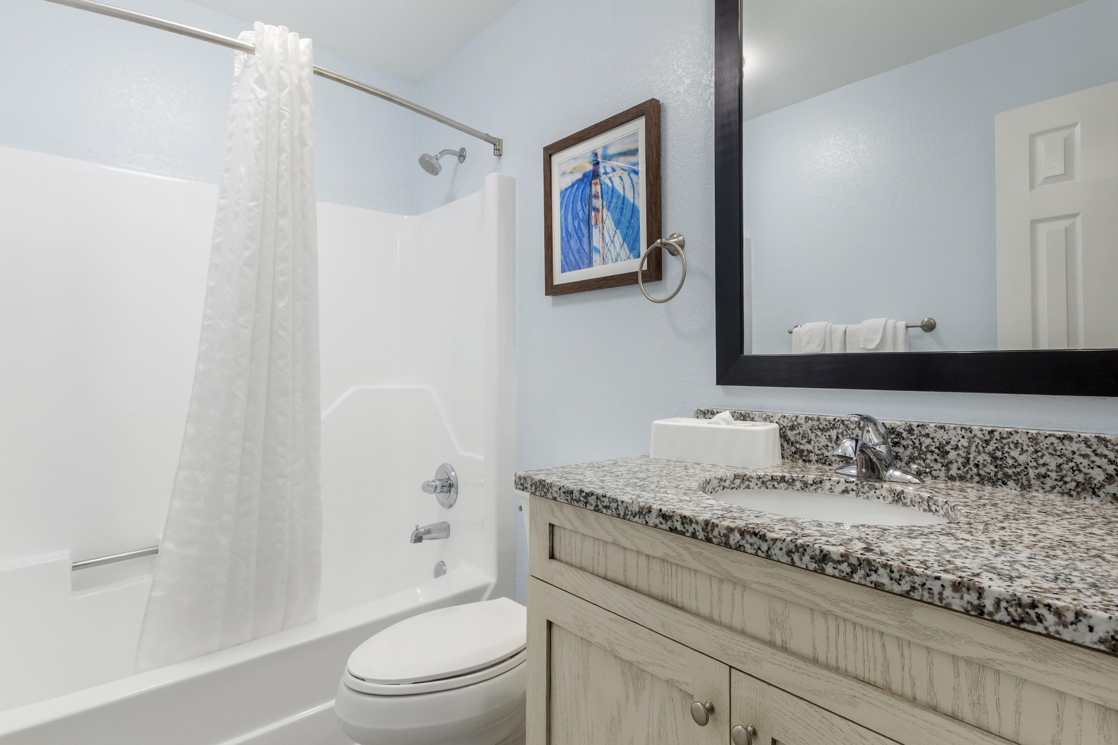 A bathroom with a shower, toilet, sink, and a mirror.