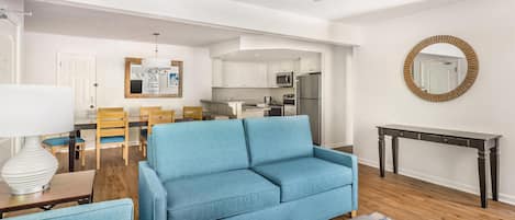 A modern living room with a blue sofa, wooden dining table, and a ceiling fan.