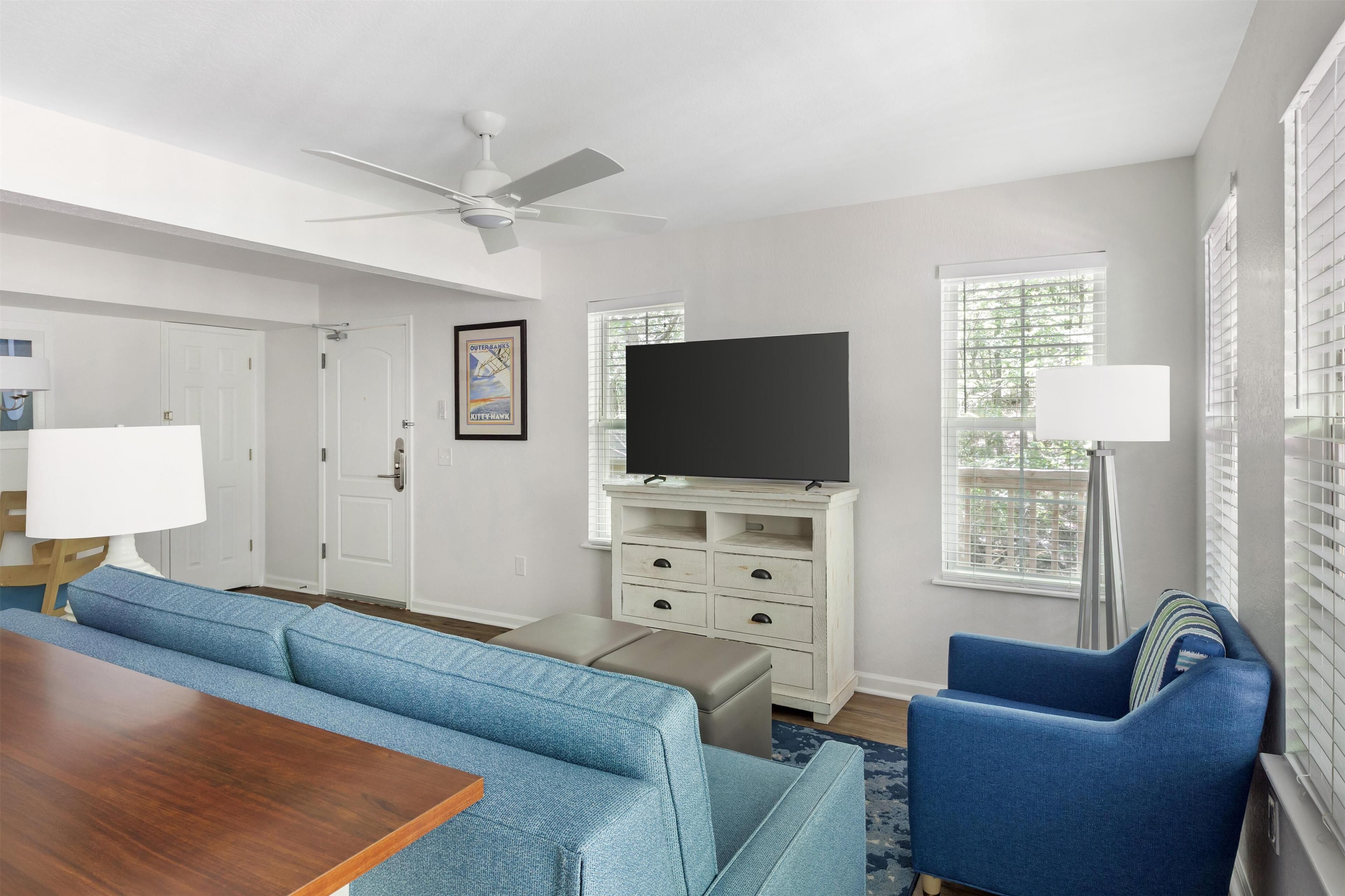 A modern living room with a sofa, a coffee table, a TV on a white stand, and a ceiling fan.
