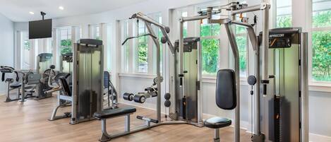 A modern gym with various exercise machines, large windows, and a flat-screen TV.