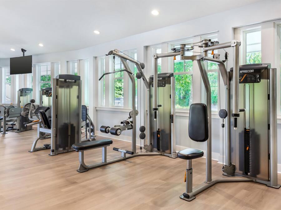 Ein modernes Fitnessstudio mit verschiedenen Trainingsgeräten, großen Fenstern und einem Flachbildfernseher.