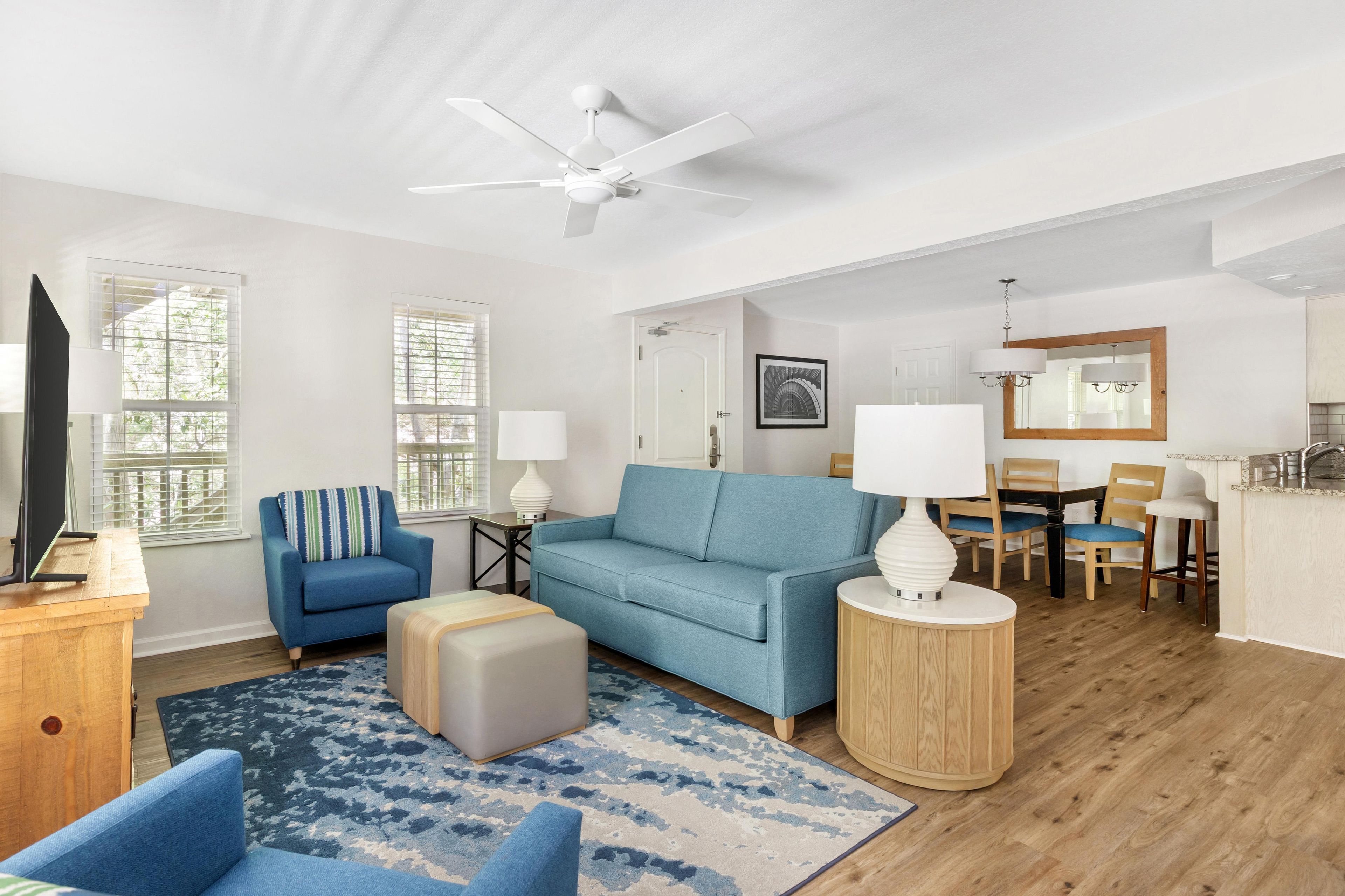 A modern living room with a blue sofa, a coffee table, a TV, and a ceiling fan.