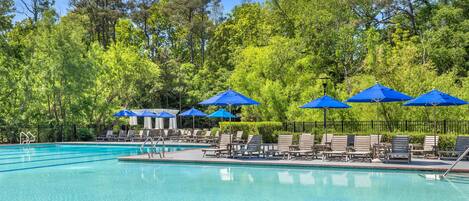 A swimming pool with blue umbrellas and lounge chairs, surrounded by trees.