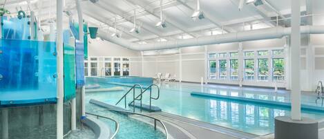 En indendørs swimmingpool med krystalklart vand, et omklædningsområde og store vinduer der lukker naturligt lys ind.