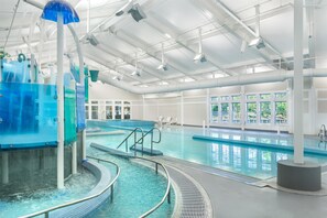 An indoor swimming pool with clear water, a blue water feature, and a sunlit ceiling.