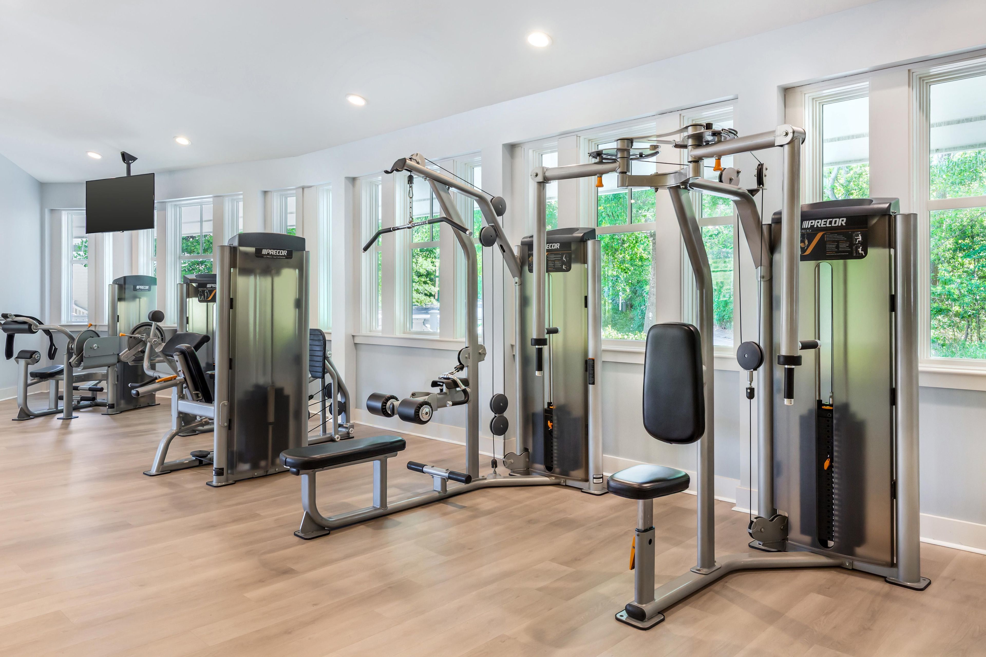 Ein Fitnessstudio mit verschiedenen Trainingsgeräten, Bänken und einem großen Fenster, das für natürliches Licht sorgt.