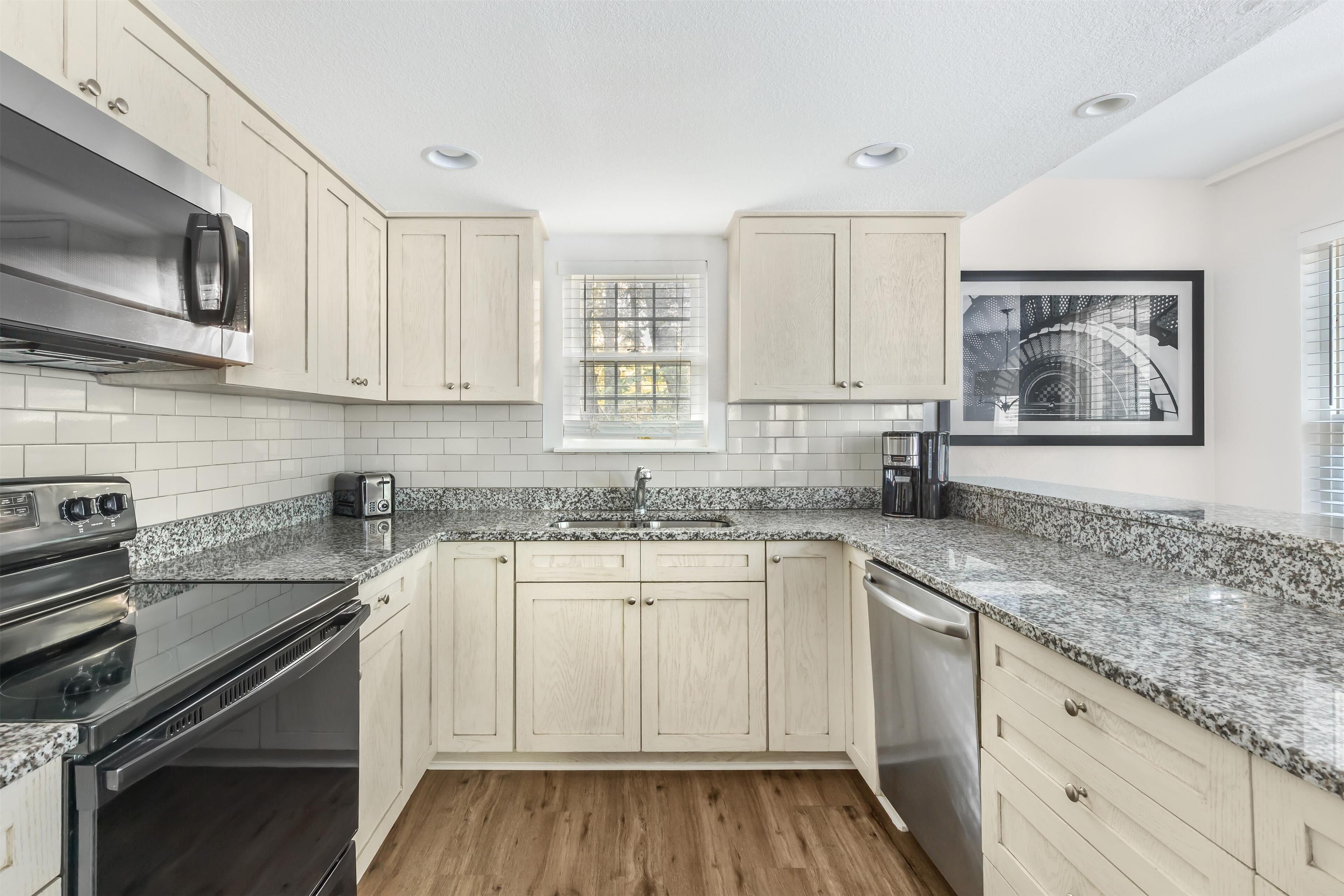 A modern kitchen with light wood cabinets, granite countertops, stainless steel appliances, and a window with a view.