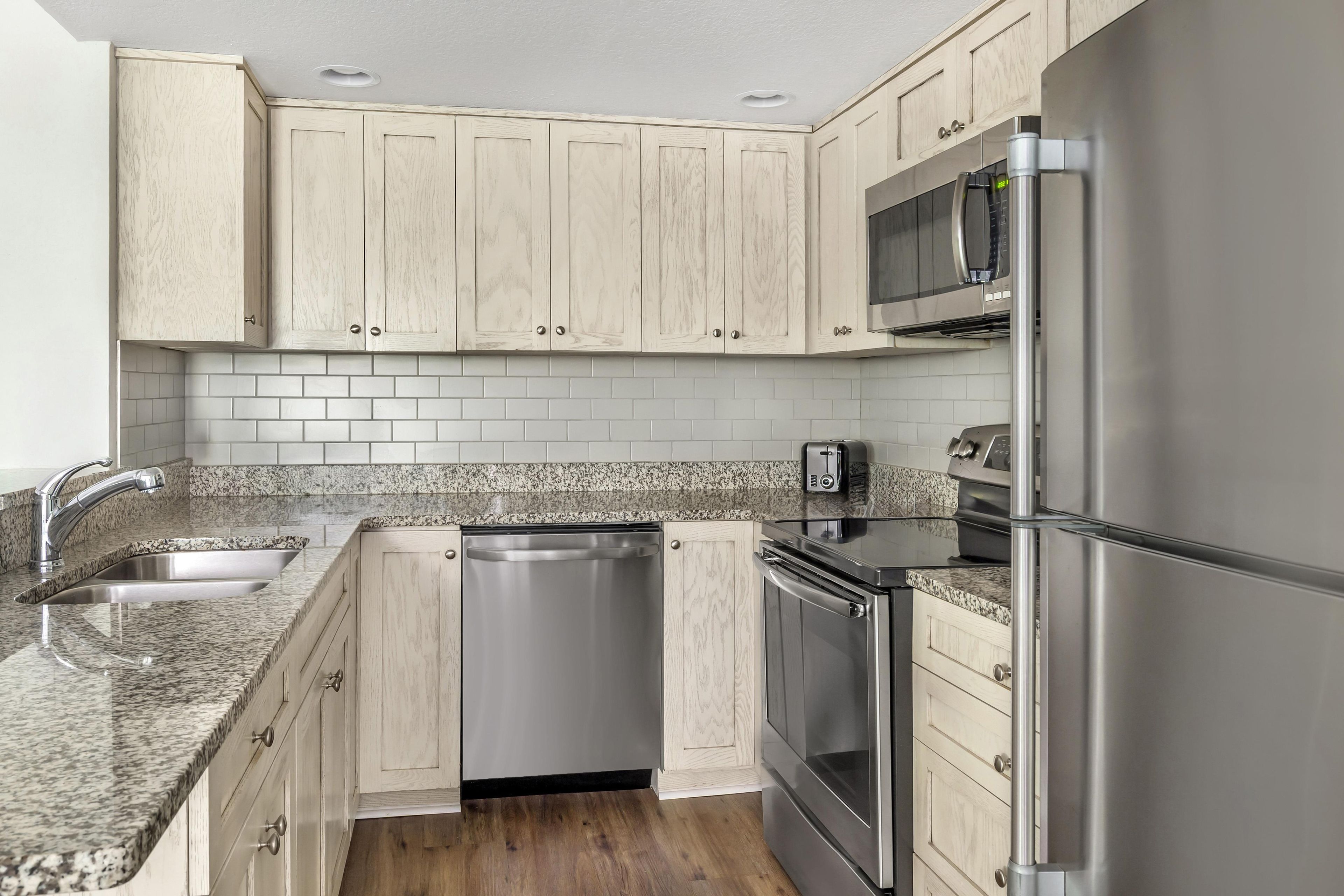 A kitchen with light wood cabinets, a stainless steel refrigerator, a microwave, a dishwasher, and granite countertops.