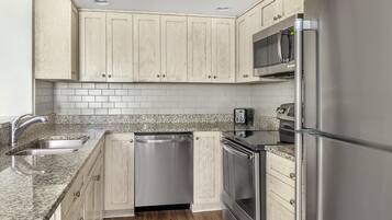 A kitchen with light wood cabinets, a stainless steel refrigerator, a microwave, a dishwasher, and granite countertops.