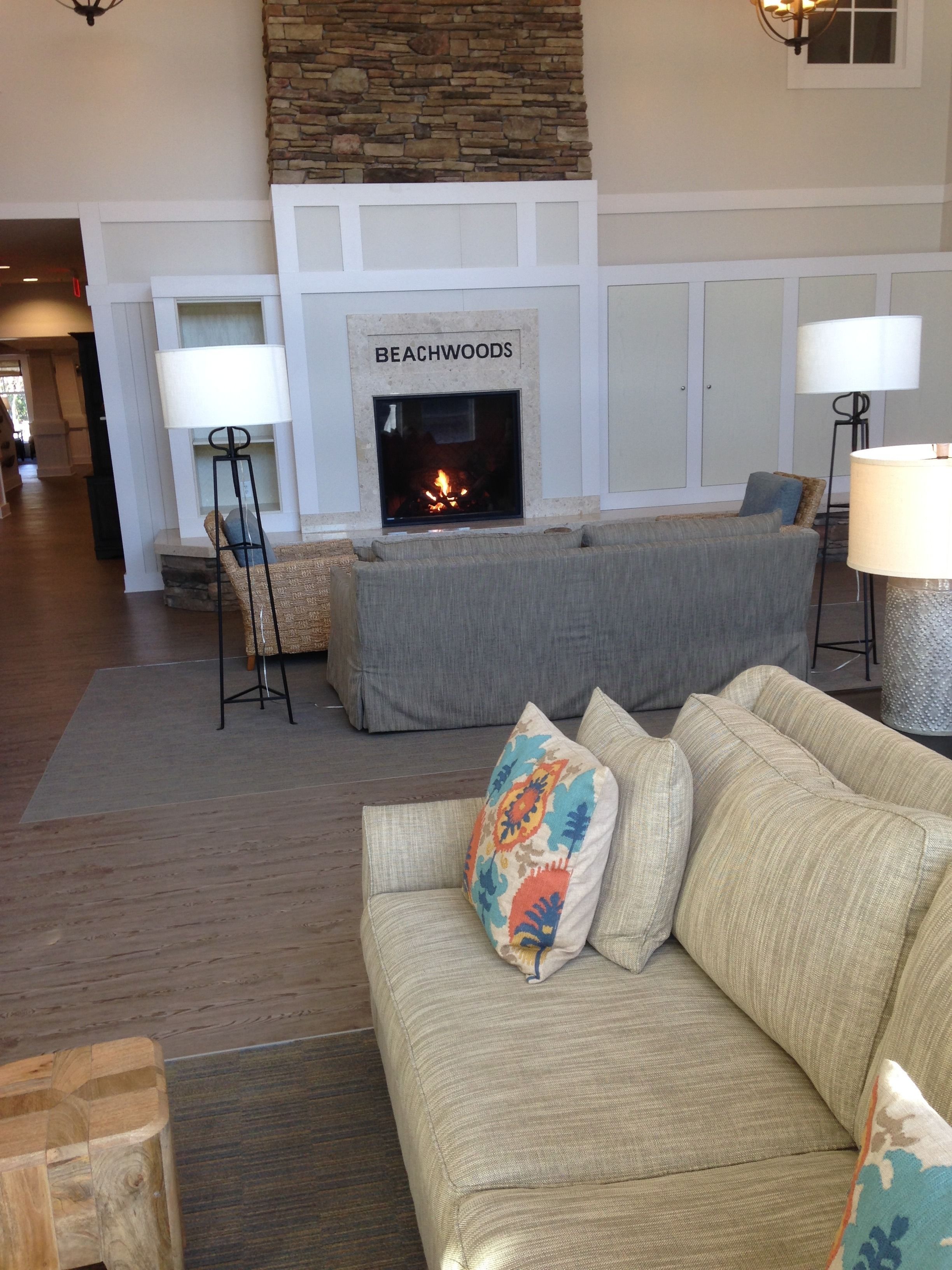 A living room with a fireplace labeled 'BEACHWOODS', a grey sofa, and a beige sofa with colorful pillows.