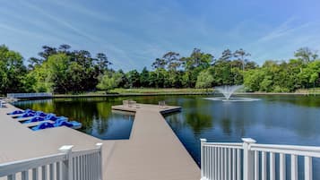 A wooden dock with benches and blue paddle boats, leading to a calm lake with a fountain.