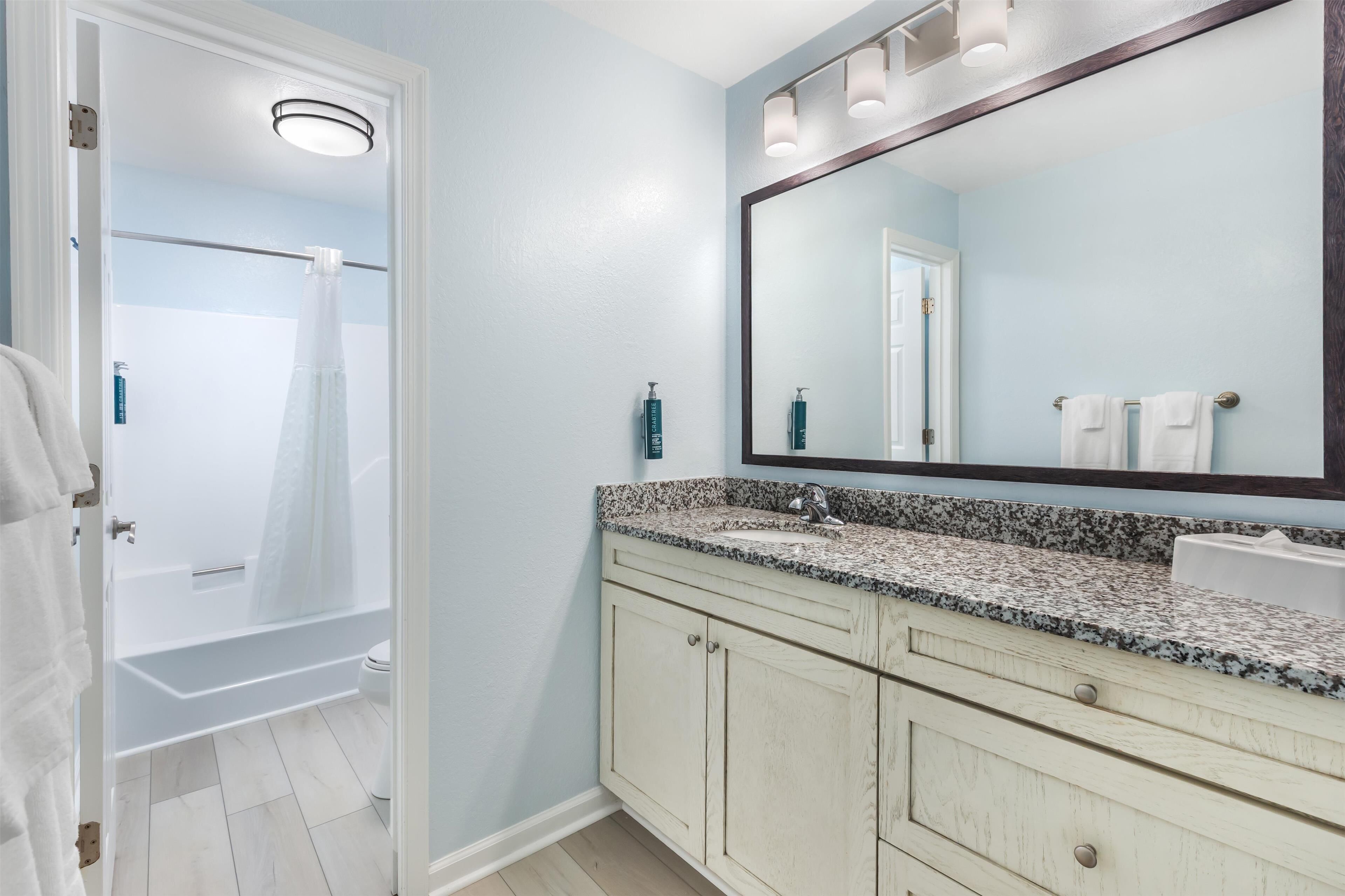 A bathroom with a shower, a sink with a mirror, and a vanity with cabinets.