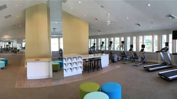 Een fitnessruimte met loopbanden, hometrainers en een receptie met kleurrijke krukken.