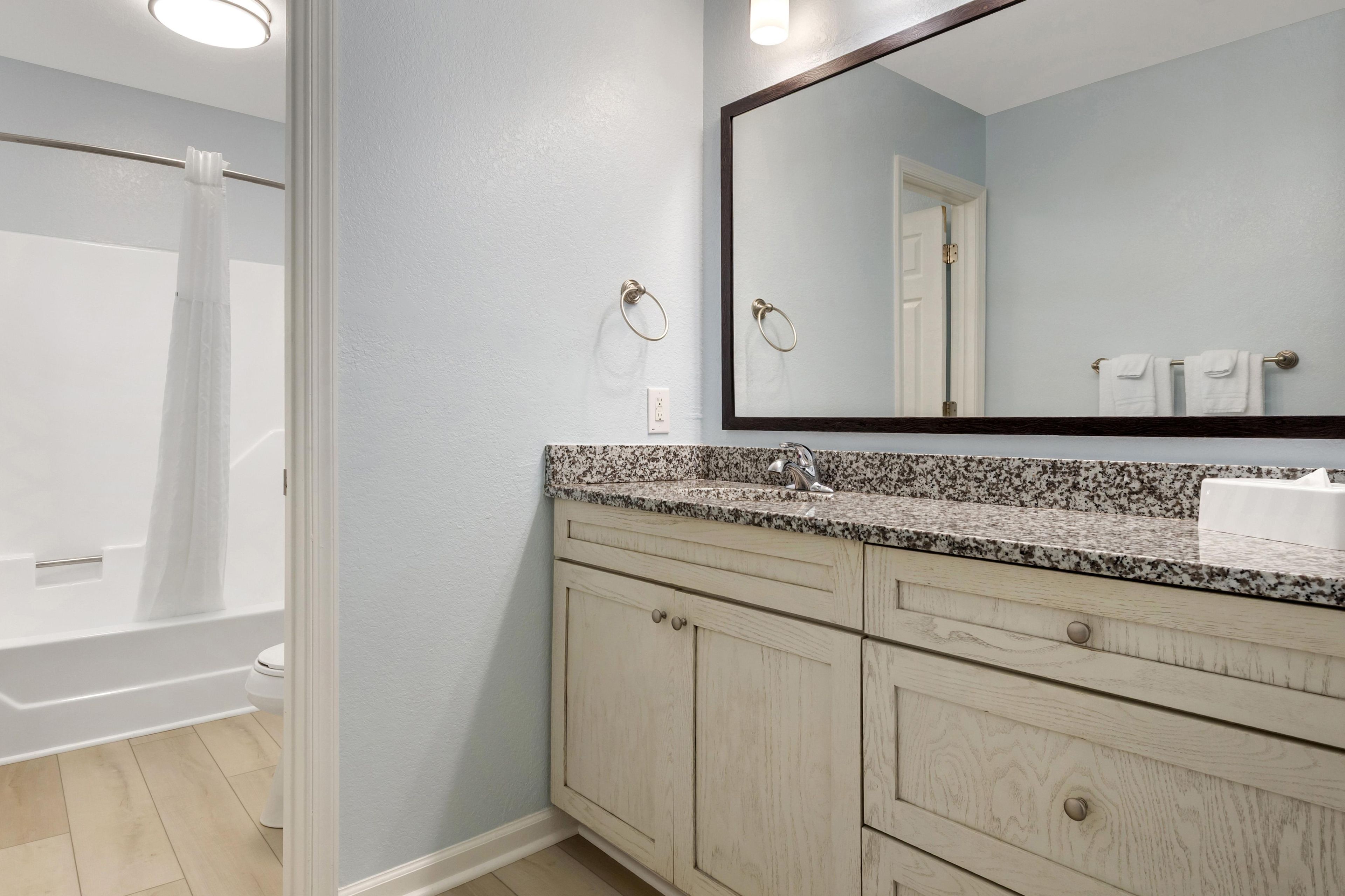 A bathroom with a shower, a sink with a granite countertop, and a mirror.