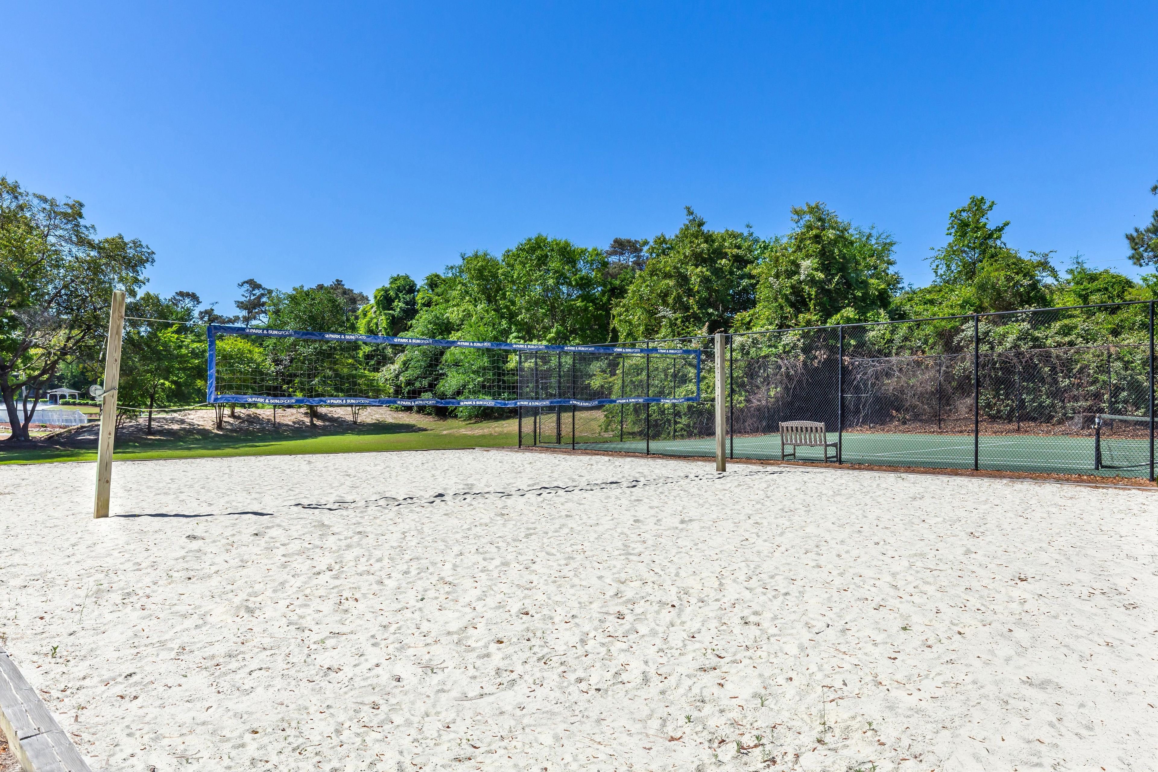 A sandy beach volleyball court with a net, surrounded by trees and a fence.