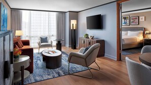 A modern hotel room with a flat-screen TV, a sofa, a round coffee table, a bed, and a small side table.