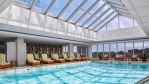 An indoor swimming pool with multiple lounge chairs and a skylight.
