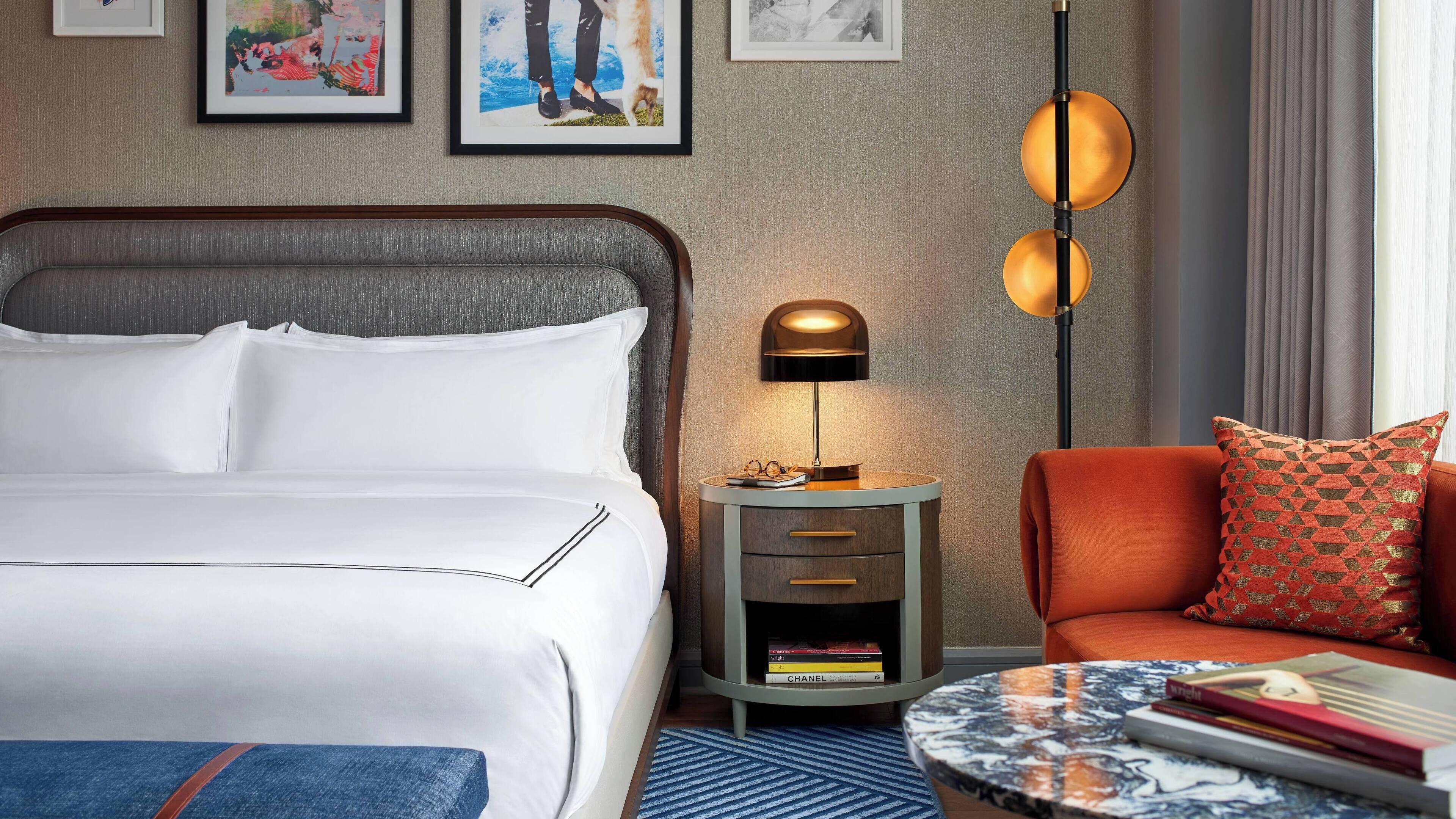 Een hotelkamer met een bed, een nachtkastje met een lamp, een stoel en een klein tafeltje met boeken.