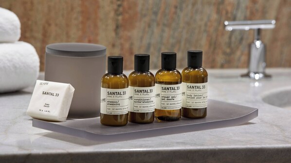 A bathroom with a marble countertop, a large mirror, and four bottles of Santal 33 body lotion.