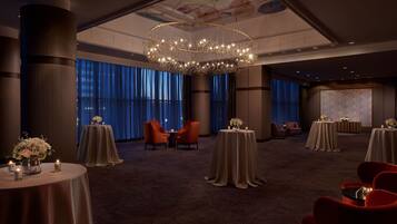 A spacious hotel lobby with a large chandelier, multiple round tables with floral centerpieces, and comfortable seating areas.