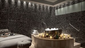 A spa room with a massage table, a circular hot tub, and candles.