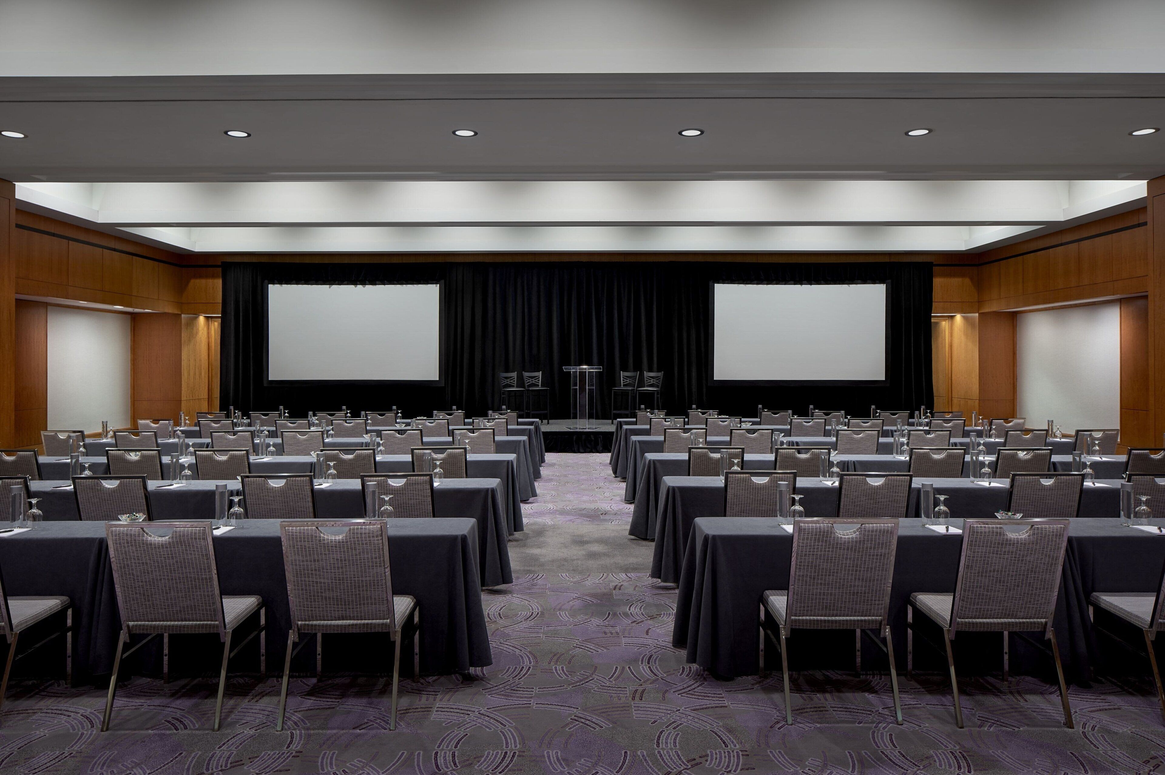 A conference room with rows of tables and chairs, a stage with a screen, and a podium.