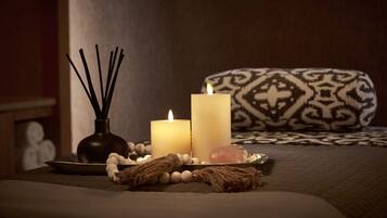 Una habitación con una cama, dos velas, un florero con palitos de juncos, un cojín decorativo y una bandeja con diversos objetos.
