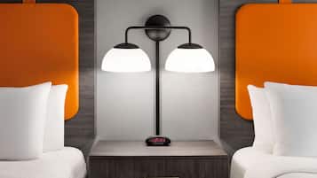 Quarto de hotel moderno com duas camas, uma mesa de cabeceira e uma luminária na parede.