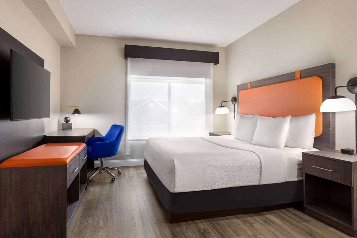 Une chambre d’hôtel équipée d’un lit, d’un bureau, d’une chaise et d’un téléviseur fixé au mur.