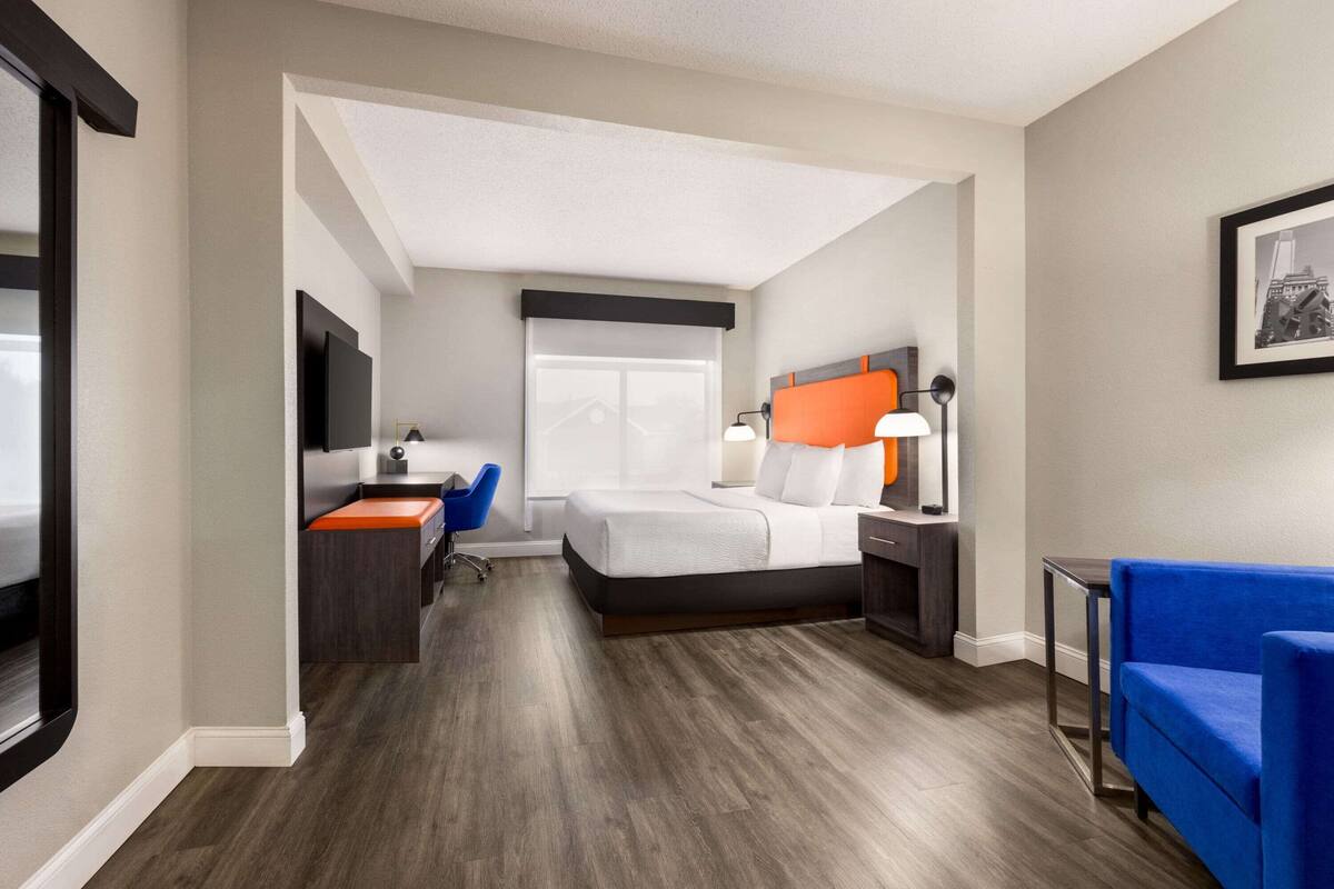Une chambre d’hôtel avec un lit, un bureau, une chaise, une télévision et un canapé bleu.