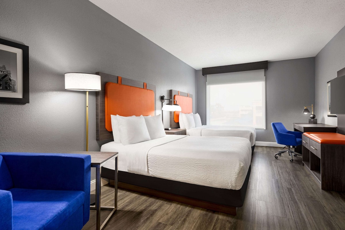 Une chambre d’hôtel avec deux lits, un bureau, une chaise et une grande fenêtre.