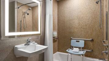 Un baño con lavabo, espejo, ducha y un banco accesible para sillas de ruedas.
