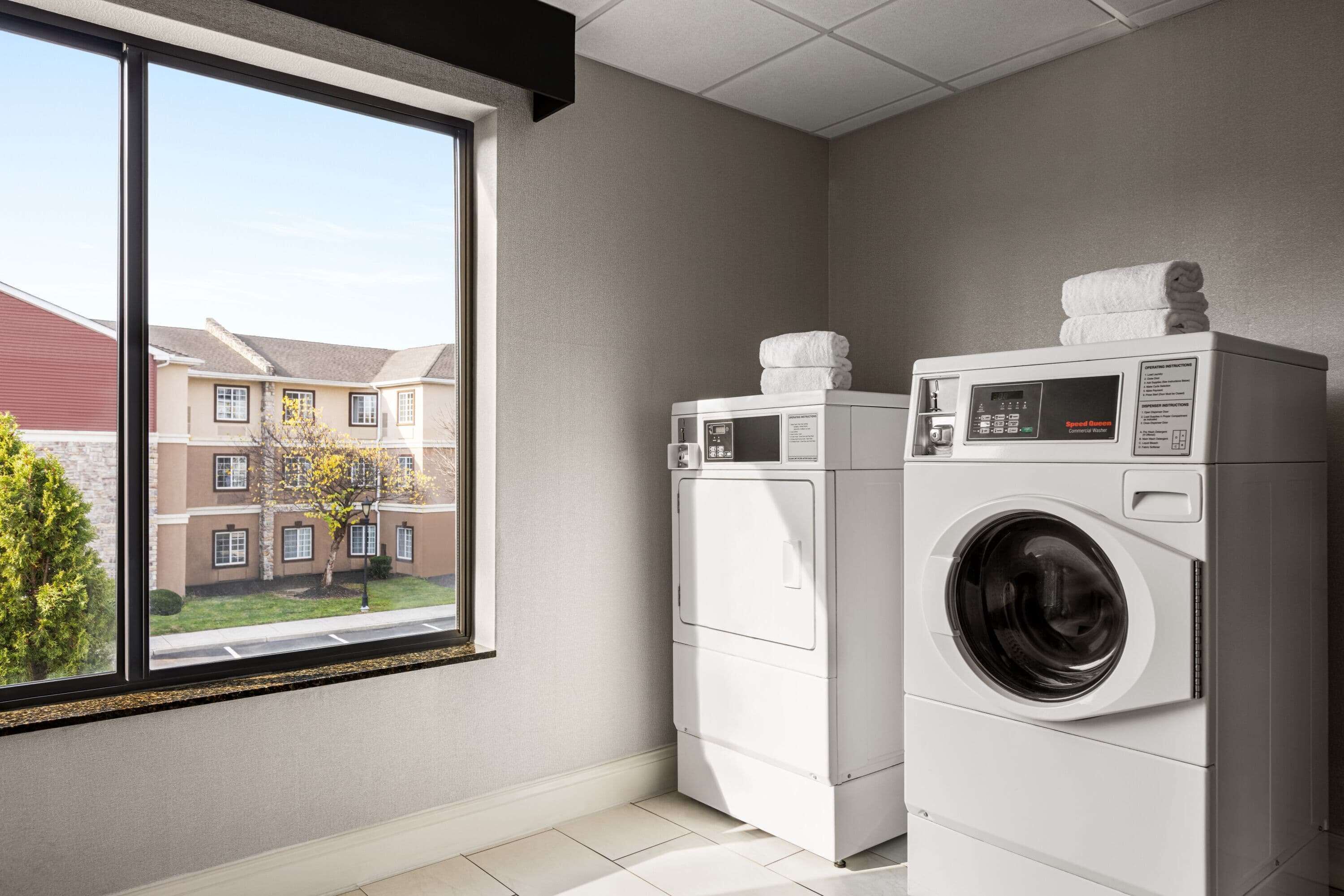 A laundry room with two stacked washers and dryers, a large window with a view of a residential area.