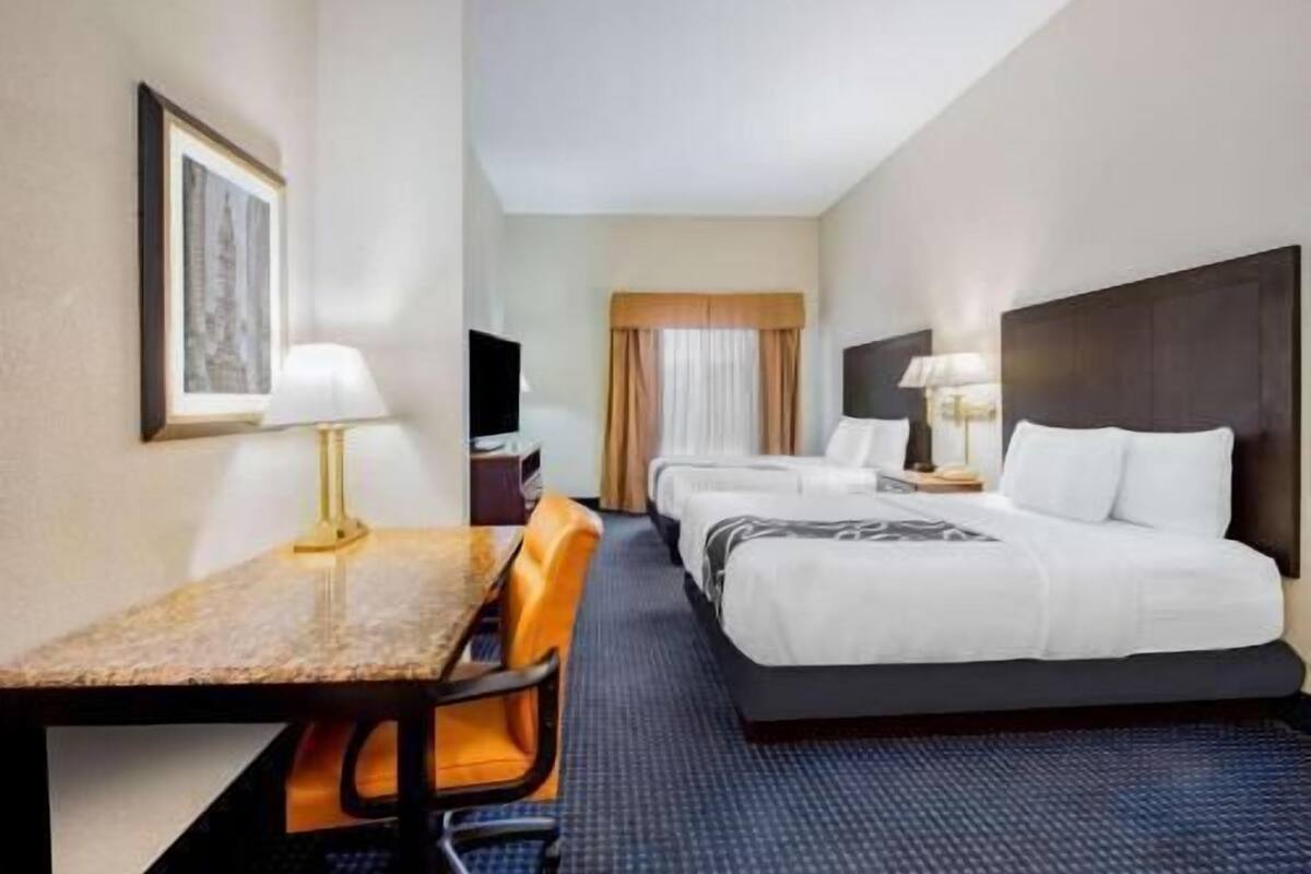 Une chambre d’hôtel avec un lit, un bureau, une chaise, une télévision et une fenêtre avec des rideaux.