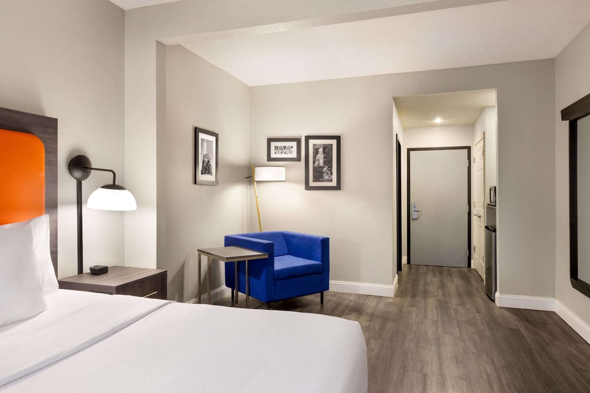 Une chambre d’hôtel avec un lit, un bureau, une chaise, une lampe et des tableaux encadrés au mur.